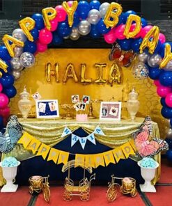 Vibrant birthday party setup featuring a blue, pink, and silver balloon arch with 'Happy Birthday' foil balloon, personalized name balloons, balloon pillars with number foil balloons, a decorated table with 'Happy Birthday' bunting, and 50 balloon bunches around the venue.